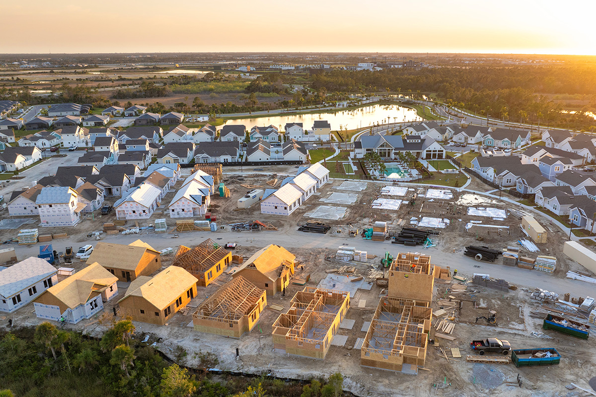 Aerial view of a new single-family home community with framing in progress and finished homes around a small lake at sunset.