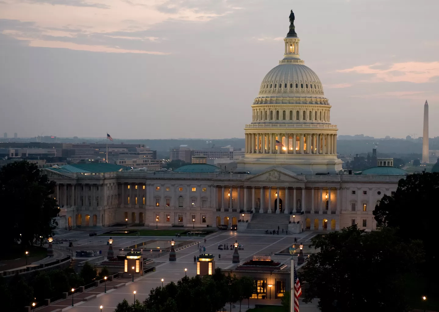 The United States Capitol at dusk, with the dome lit and the Washington Monument visible in the distance.